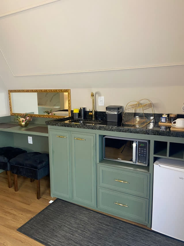 Kitchenette de armários verdes com micro-ondas, frigobar e bancada de trabalho