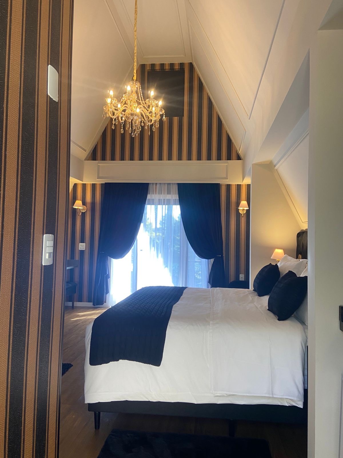 Cama king size do chalé com papel de parede listrado e lustre de cristal