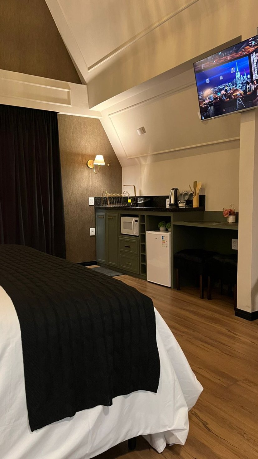Chalé visto da cama, com a kitchenette e a televisão ao fundo