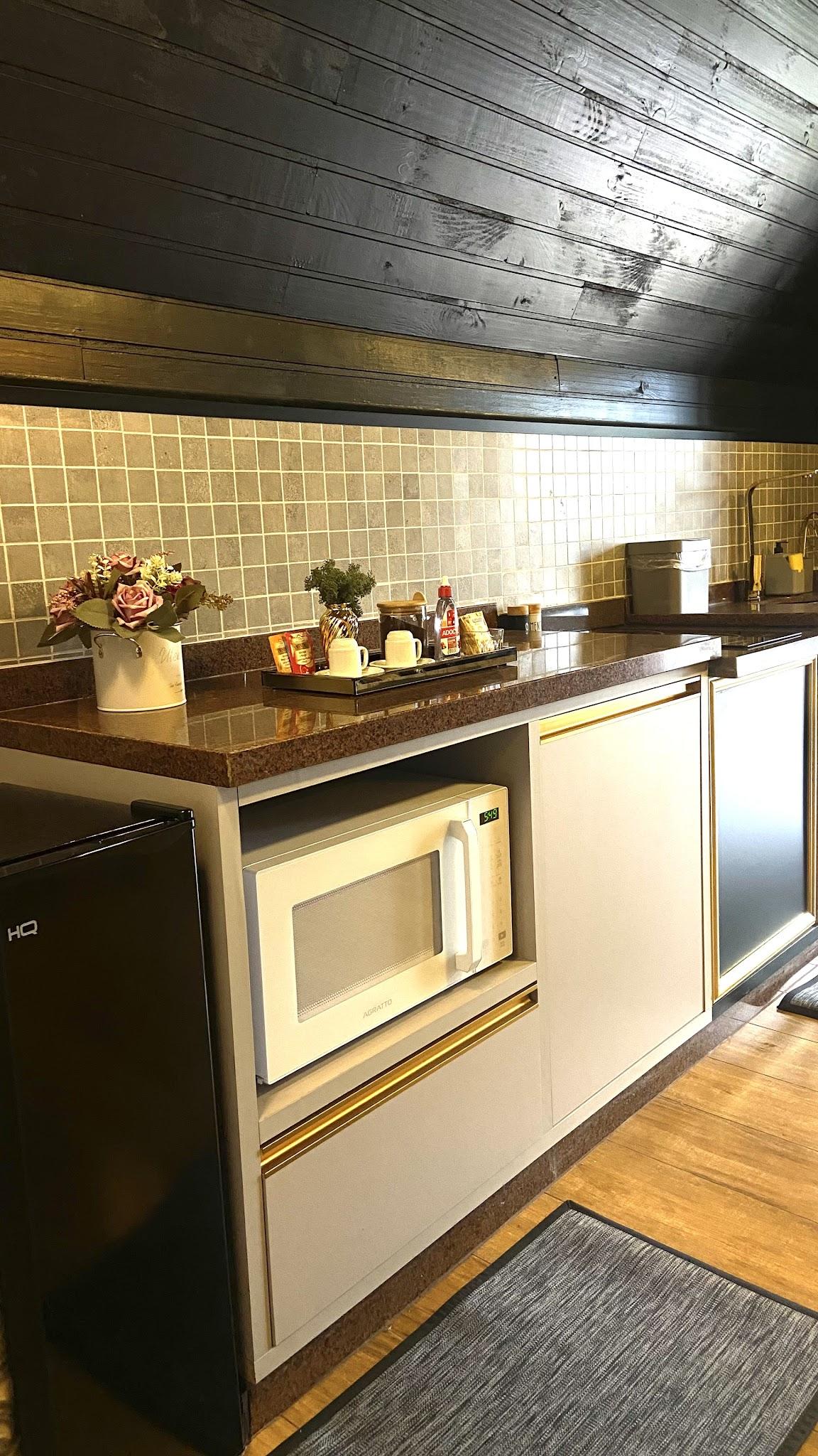 Cozinha do Chalé Duplex com micro-ondas, bancada de madeira e revestimento claro