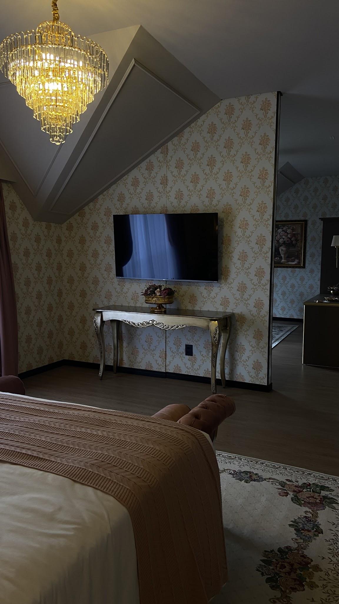Televisão e aparador da Suíte Imperial vistos da cama, sob lustre de cristal