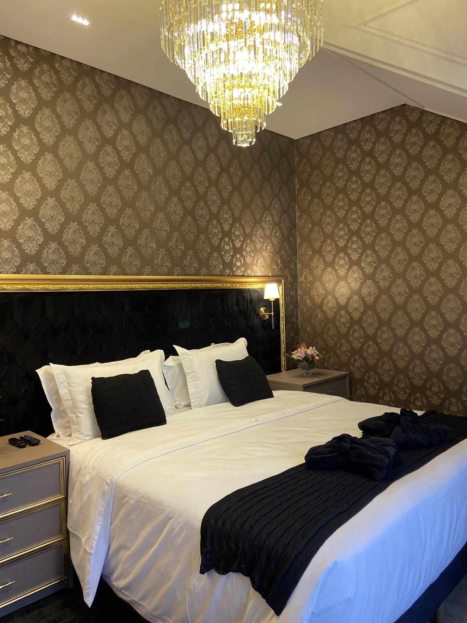 Suíte Majestic com papel de parede dourado, cabeceira preta e lustre de cristal