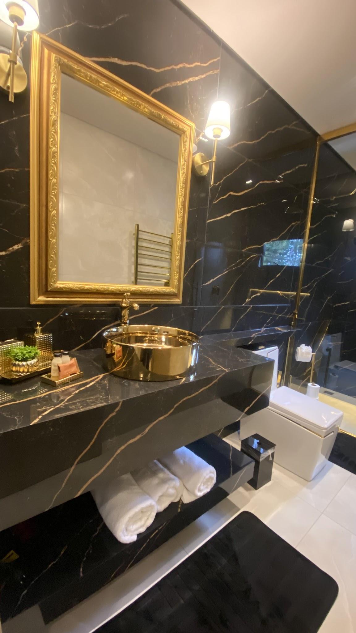 Bancada de mármore preto da Suíte Majestic com cuba dourada e toalhas dobradas