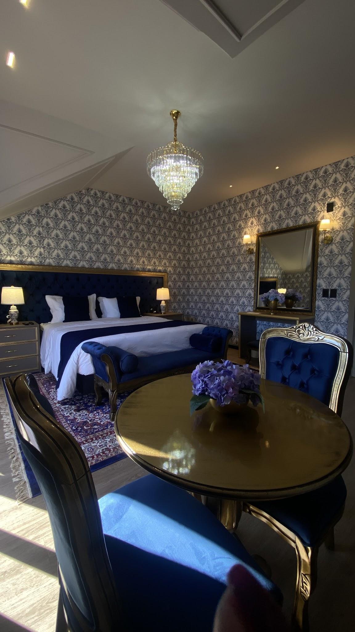 Cama king size da Suíte Royale com cabeceira azul, mesa de jantar e lustre de cristal
