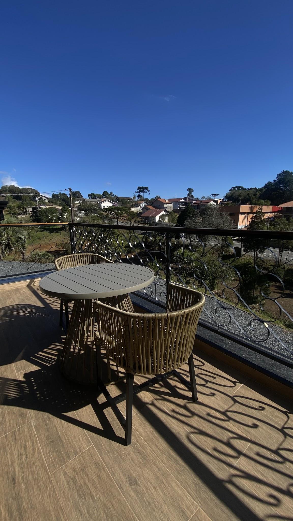 Varanda da Suíte Royale com mesa, cadeiras de corda e vista aberta sobre o bairro e as araucárias