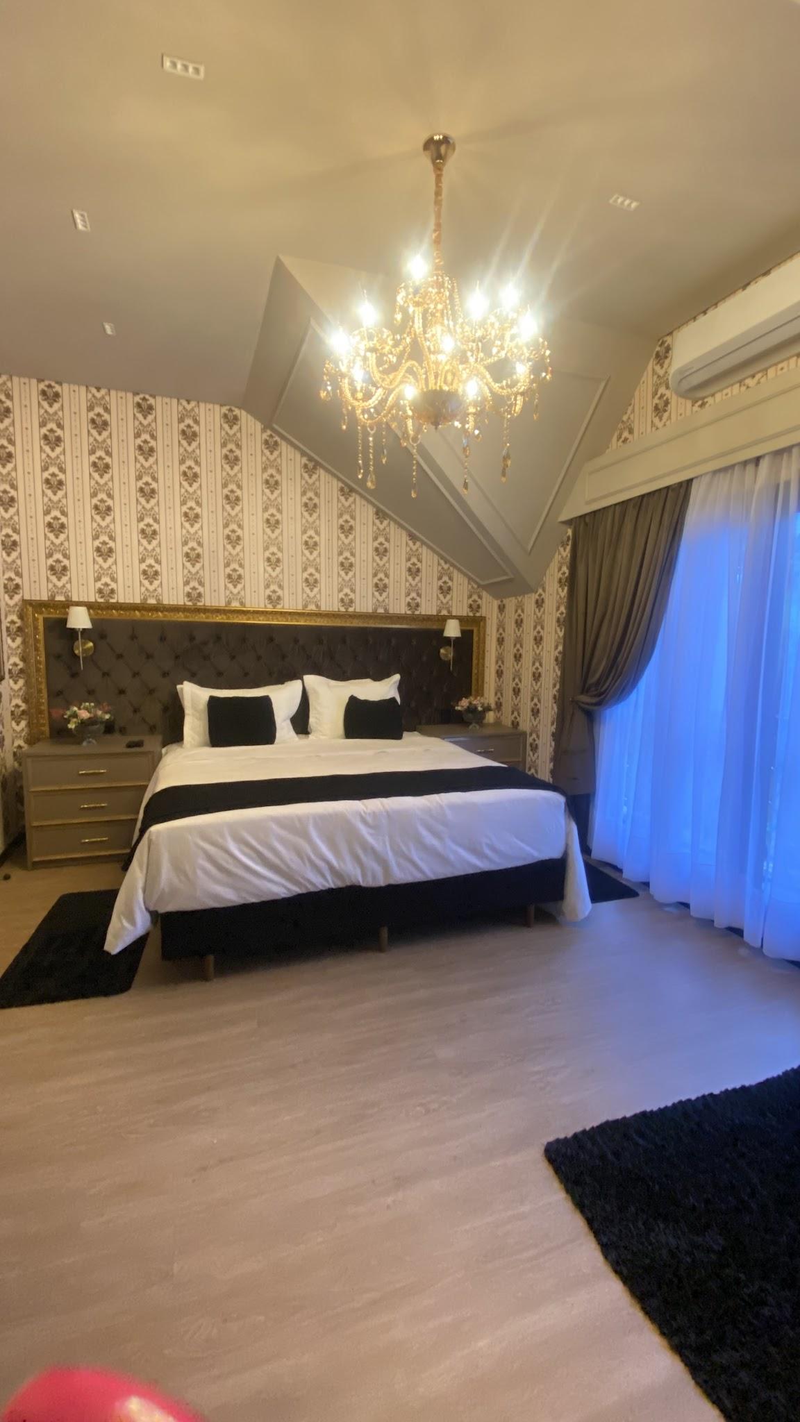 Cama king size da Suíte Versailles com cabeceira escura, lustre de cristal e cortina clara
